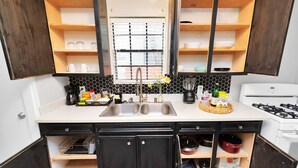 A kitchen with a double sink, black cabinets, a gas stove, and a window with blinds.