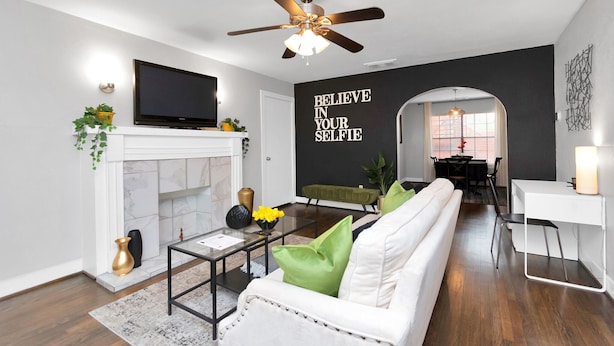 A modern living room with a fireplace, white sofa, and a motivational wall quote.