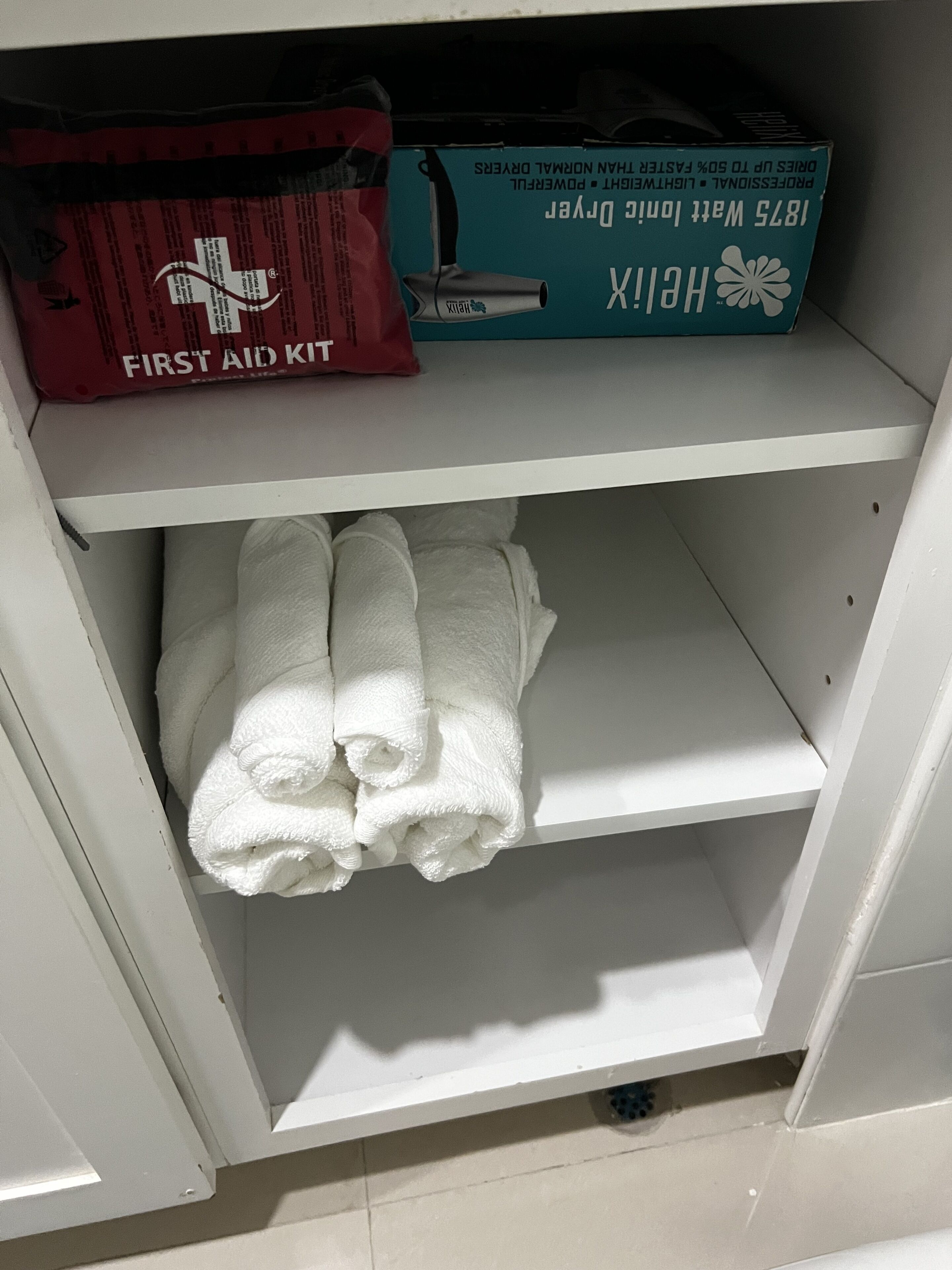 A storage area with a first aid kit, a hairdryer, and neatly folded towels.