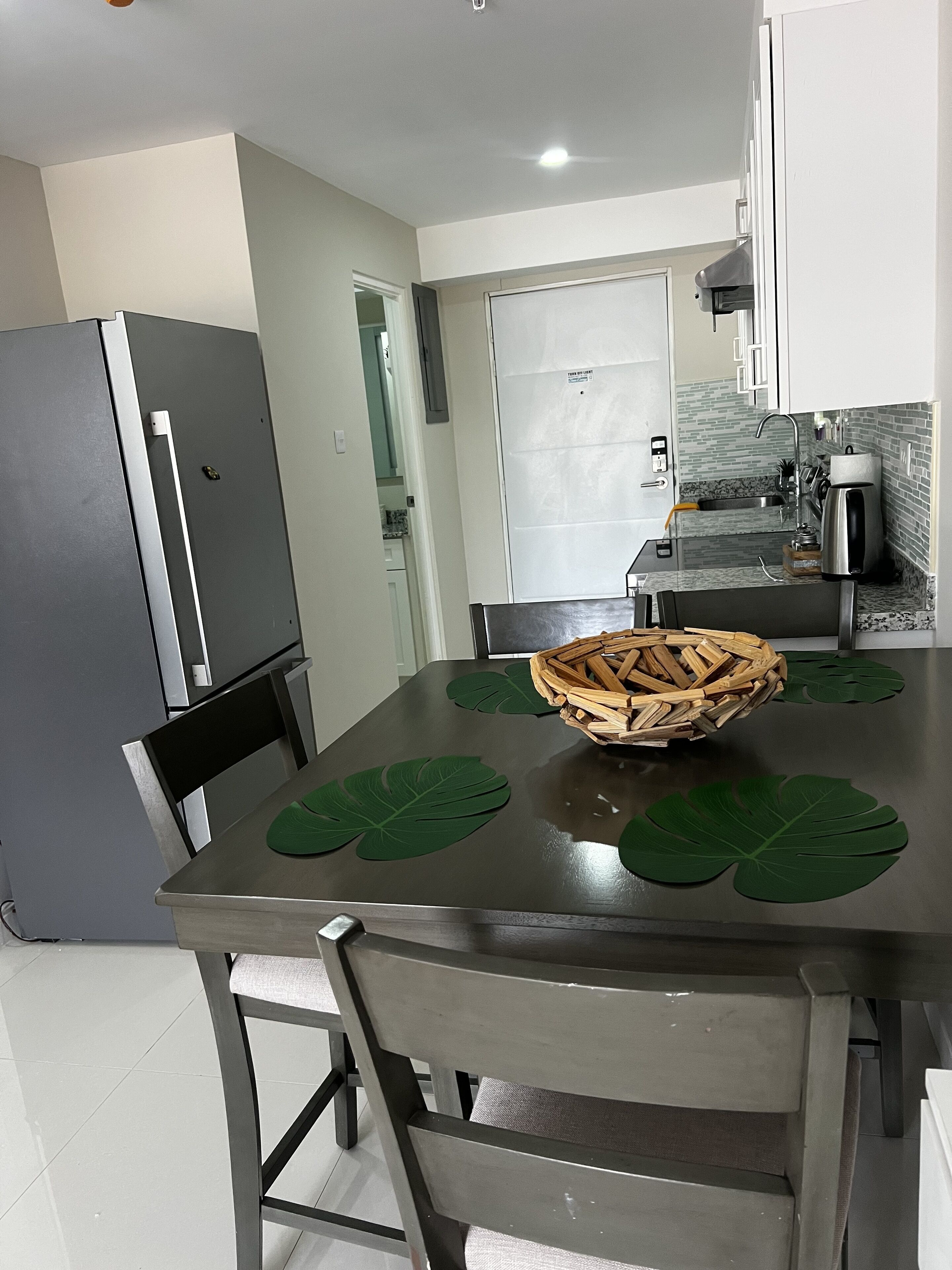 Une cuisine moderne avec un réfrigérateur en acier inoxydable, une table à manger agrémentée d’un centre de table en forme de panier tressé, et un îlot de cuisine doté d’un évier et d’une machine à café.