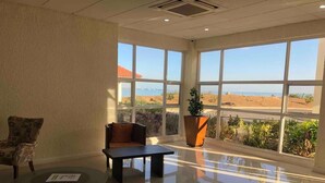 A spacious lobby with a large window offering a view of a beach and desert landscape. - AC, WiFi, cable & 24/7 security, Pool, beachfront, views of Kingston harbor. (Portmore)
