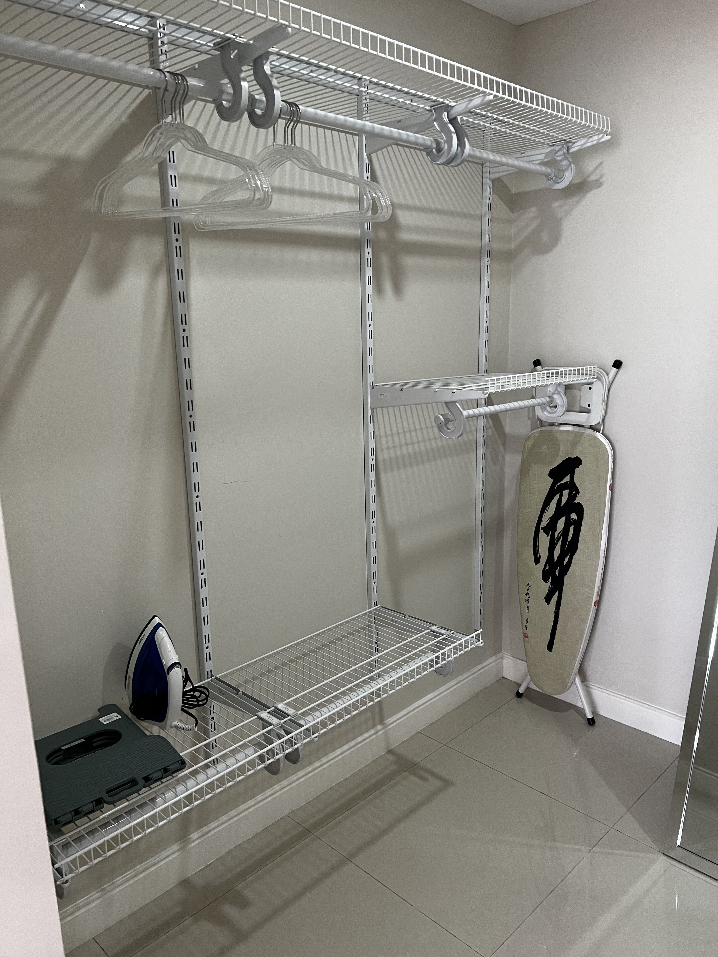 A storage closet with metal shelves, an ironing board, and a vacuum cleaner.