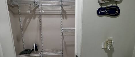Un dressing avec des étagères en métal, un fer à repasser et un porte-serviettes fixé au mur.