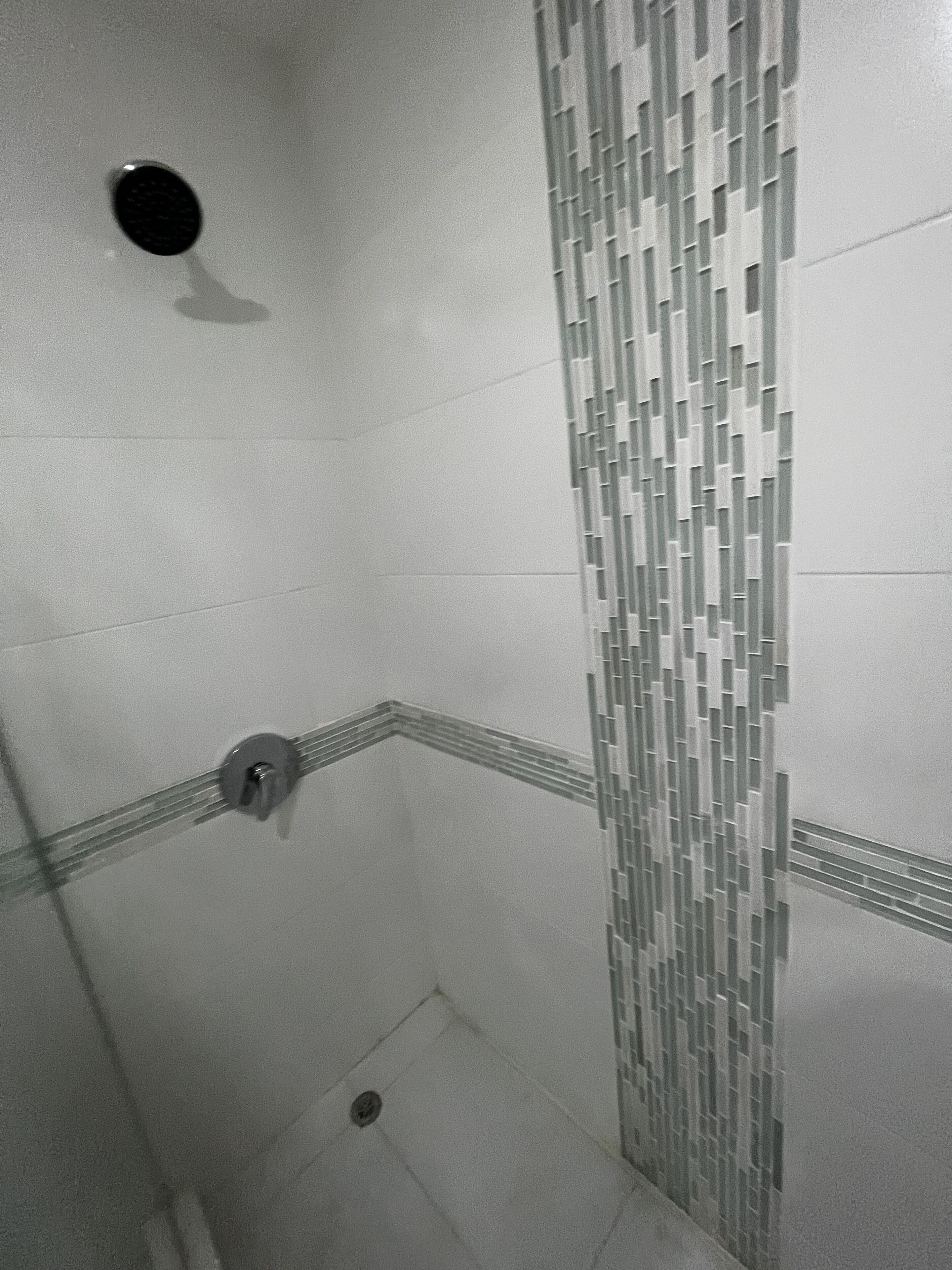 Een douche met een betegelde wand en een afvoer.