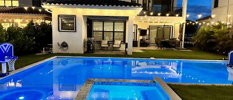 A modern house with a swimming pool, outdoor seating, and string lights.
