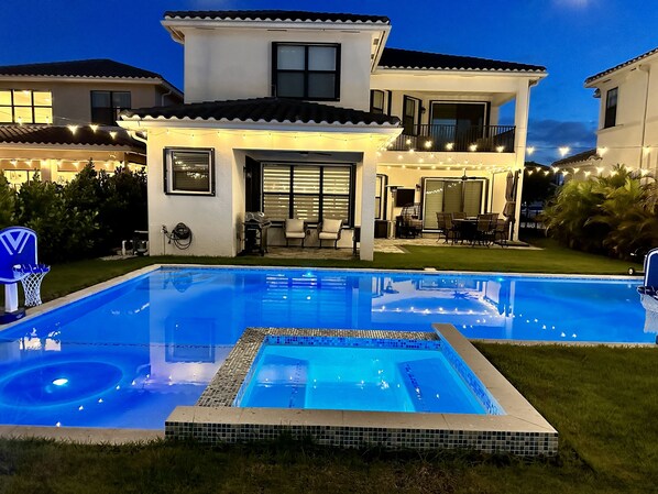 Una casa moderna con piscina, mobiliario exterior e iluminación colgante.