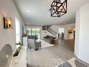 Un amplio salón con una escalera moderna, un sofá grande y una lámpara decorativa en el techo.