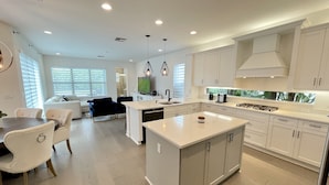 A modern kitchen with white cabinetry, a central island, and a dining area with a table and chairs.