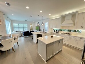 Una cocina moderna con armarios blancos, una isla central y un comedor con mesa y sillas.