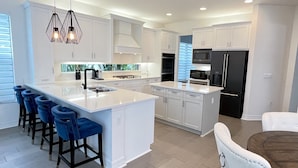 A modern kitchen with white cabinetry, a large island with bar stools, and built-in appliances.