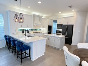 Una cocina moderna con armarios blancos, una isla grande con taburetes y electrodomésticos integrados.