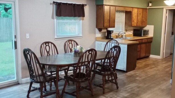 A dining area with a round table and six chairs, a kitchen with wooden cabinets, and a "Blessed" sign on the wall. - short walk to Ball State University Campus - Quiet Neighborhood (Muncie)