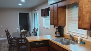 A compact kitchen with wooden cabinets, a dishwasher, a sink, and a dining area with chairs. - short walk to Ball State University Campus - Quiet Neighborhood (Muncie)