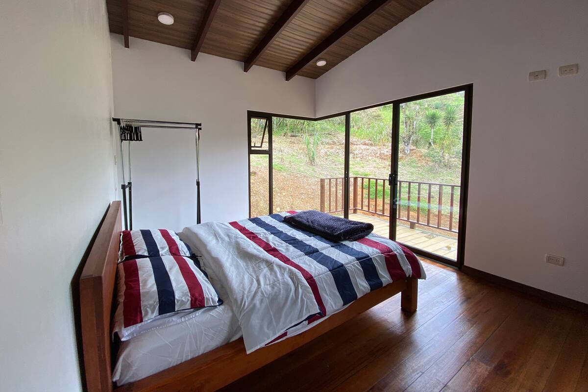 Une chambre avec un lit en bois, un ventilateur de plafond et une grande porte-fenêtre coulissante donnant sur une terrasse extérieure.