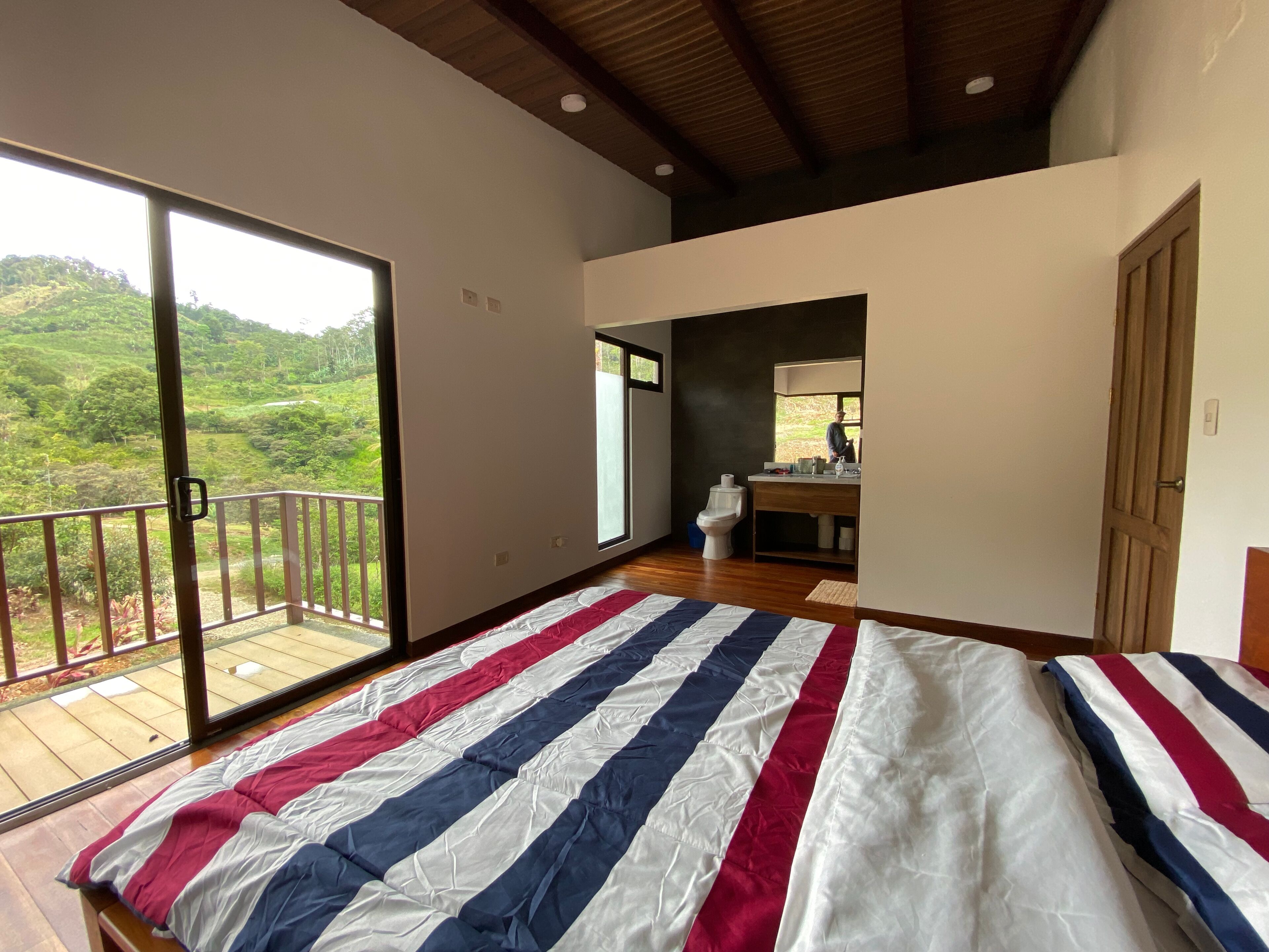 Une chambre avec un grand lit, une salle de bain et un balcon donnant sur un espace verdoyant.