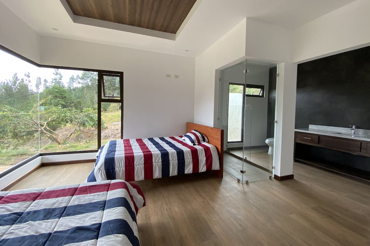 Une chambre moderne avec deux lits, une grande fenêtre et une vue sur la verdure.