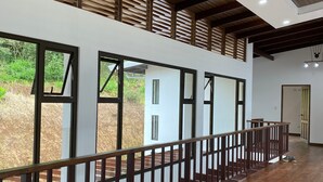 Un interior espacioso con piso de madera, ventanas grandes y una escalera con barandilla de madera.