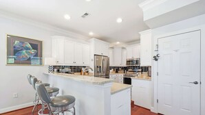 A modern kitchen with white cabinetry, stainless steel appliances, and a bar area with stools. - Sun and Games House w Swimming Pool Tons of Games Putting Green (North Myrtle Beach)