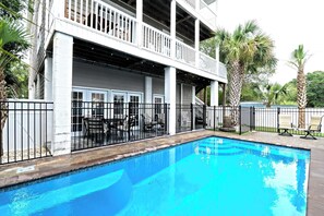Una piscina con un patio coperto, palme e un edificio con un balcone.