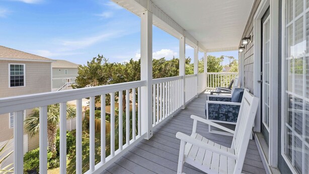 A covered porch with white railings, a bench, and a view of a residential area. - Sun and Games House w Swimming Pool Tons of Games Putting Green (North Myrtle Beach)