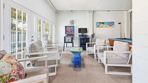 A room with white furniture, a pool table, a fan, and a television. - Sun and Games House w Swimming Pool Tons of Games Putting Green (North Myrtle Beach)