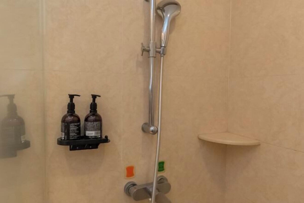 Een douche met een flexibele douchekop, een zeepdispenser aan de muur en een klein plankje.