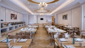 Un comedor amplio con varias mesas y sillas, una lámpara central y obras de arte en las paredes.
