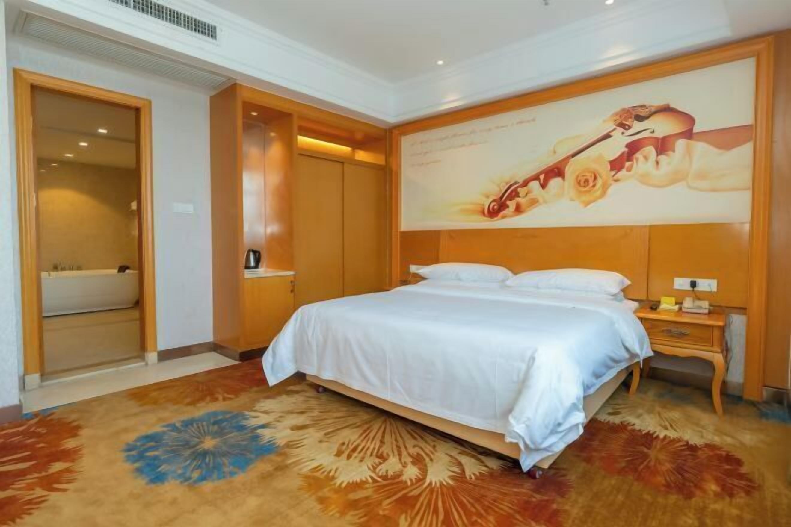 A hotel room with a bed, a nightstand, a wall-mounted TV, and a door leading to a bathroom.