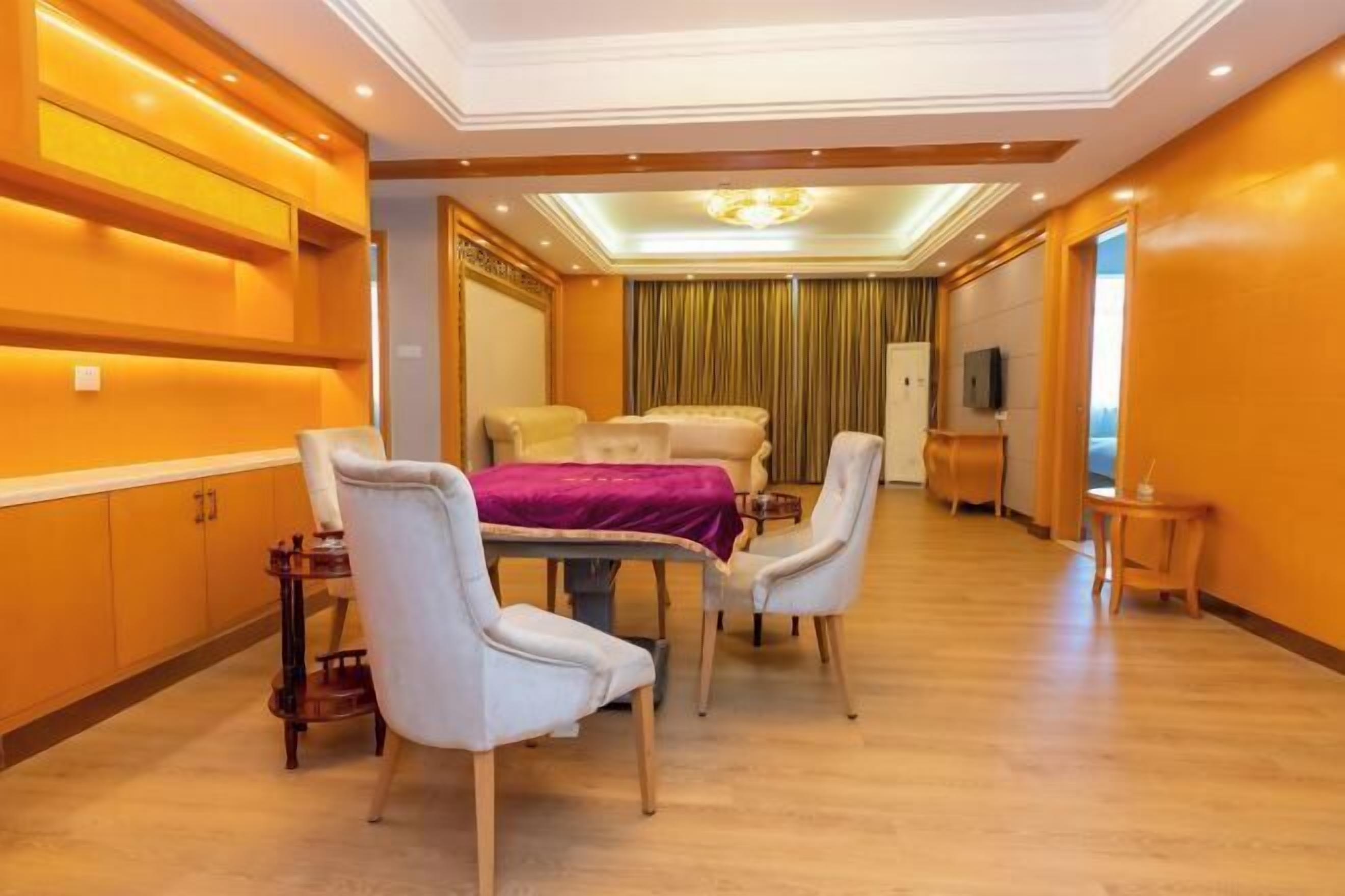 Una habitación de hotel con cama, una mesa de comedor con sillas, un televisor y una mesita de noche con lámpara.