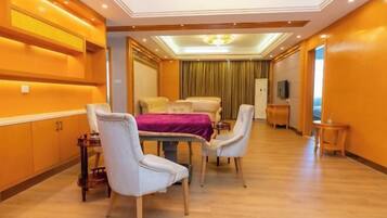 Una habitación de hotel con cama, una mesa de comedor con sillas, un televisor y una mesita de noche con lámpara.