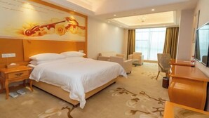 Una habitación de hotel con una cama grande, un escritorio, una silla, un televisor y un cuadro en la pared.