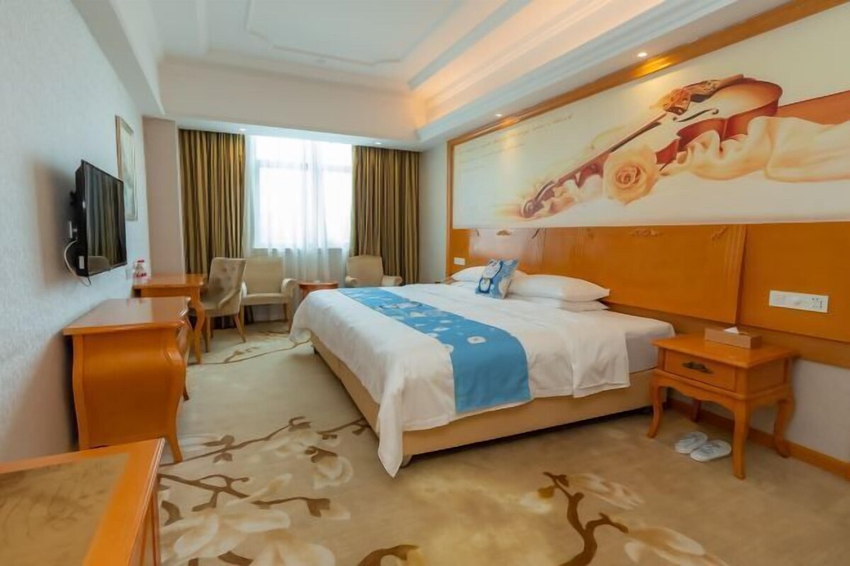 Een hotelkamer met een groot bed, een bureau, een stoel, een televisie en een schilderij aan de muur.