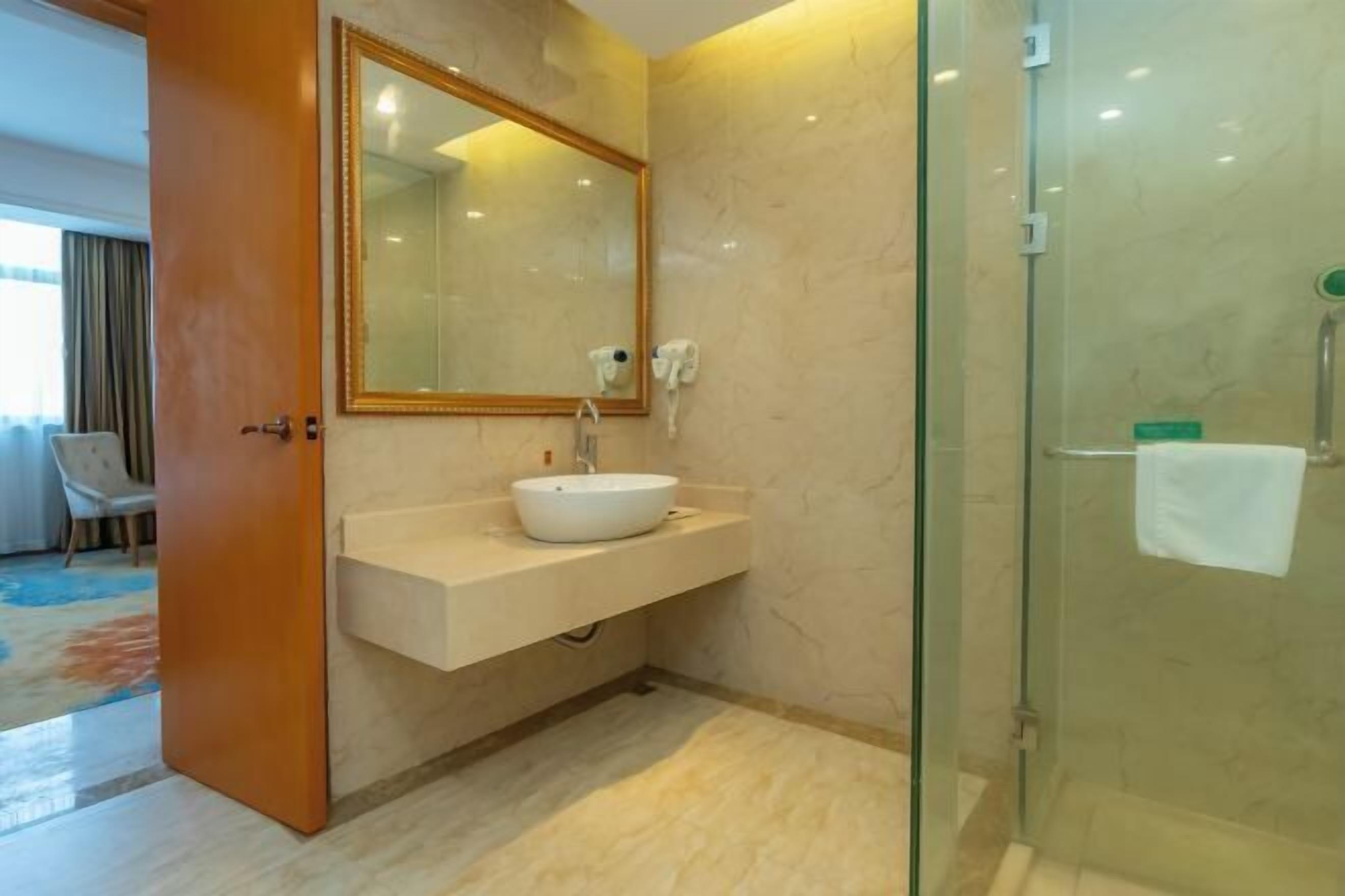 Un baño con lavamanos blanco, un espejo grande y cabina de ducha de vidrio.