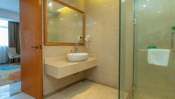 Un baño con lavamanos blanco, un espejo grande y cabina de ducha de vidrio.