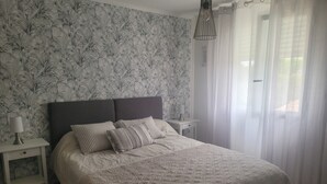 Een slaapkamer met een groot bed, twee nachtkastjes, een lamp en een raam met dunne gordijnen.