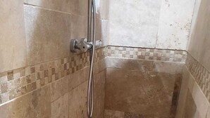 Een kleine douchecel met betegelde wanden en een handdouche.
