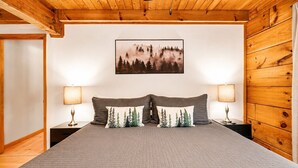 A bedroom with a bed, two nightstands, two lamps, a framed picture, and wooden walls. - Cozy Cabin- 5mins From Pigeon Forge - Hot Tub (Pigeon Forge)