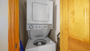 A compact washer and dryer unit in a small laundry room with a wooden door and a blue mop leaning against the wall. - Cozy Cabin- 5mins From Pigeon Forge - Hot Tub (Pigeon Forge)