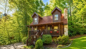 A two-story log cabin with a stone chimney, a covered porch, and a well-maintained garden. - Cozy Cabin- 5mins From Pigeon Forge - Hot Tub (Pigeon Forge)