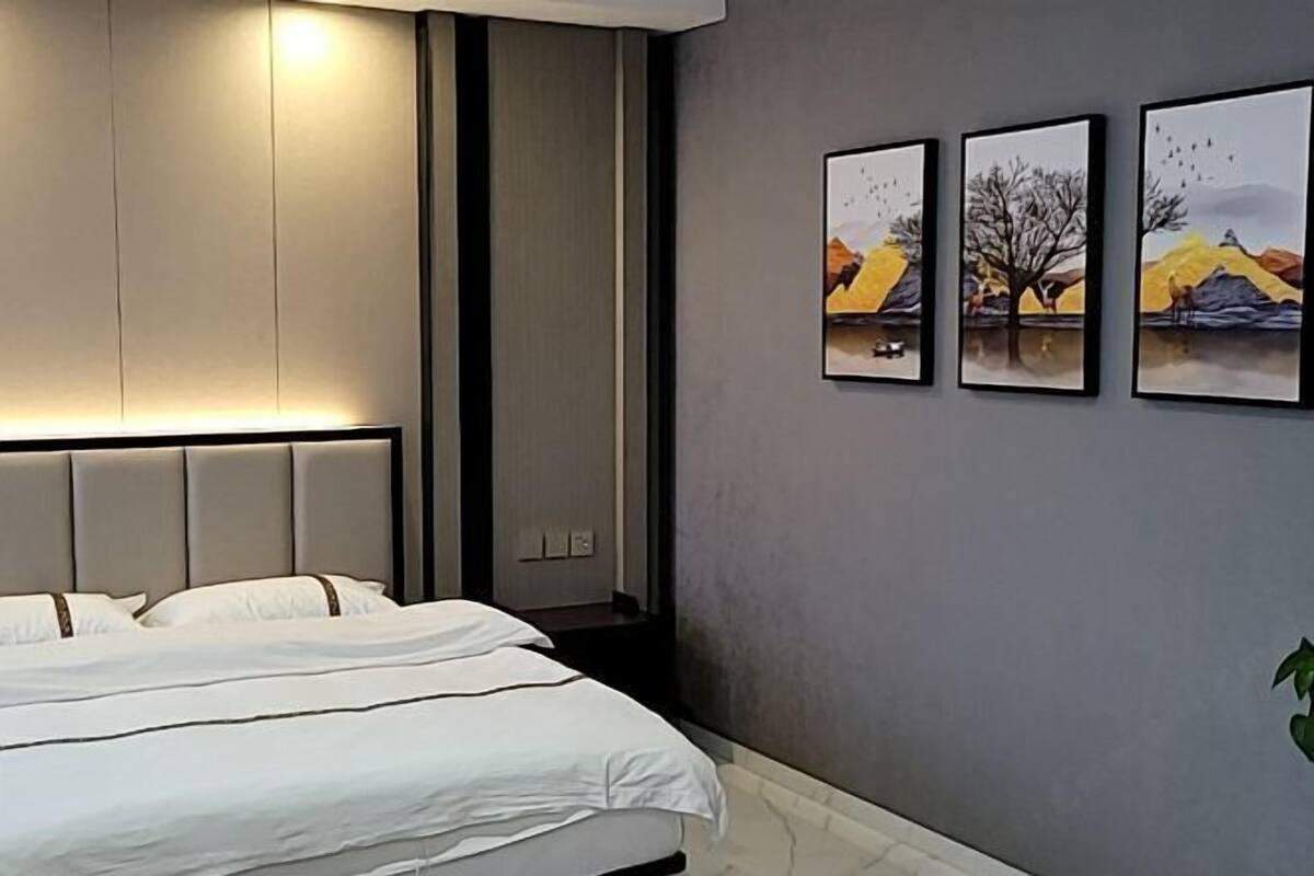 Een moderne hotelkamer met een groot bed, een hoofdeinde met ingebouwde verlichting en drie kunstwerken in lijsten aan de muur.