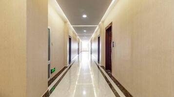 A long, narrow hotel corridor with doors on both sides, a tiled floor, and a ceiling with recessed lighting.