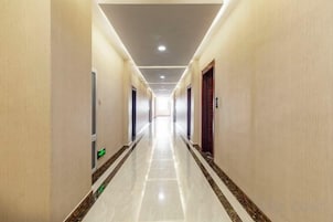 A long, narrow hotel corridor with doors on both sides, a tiled floor, and a ceiling with recessed lighting.