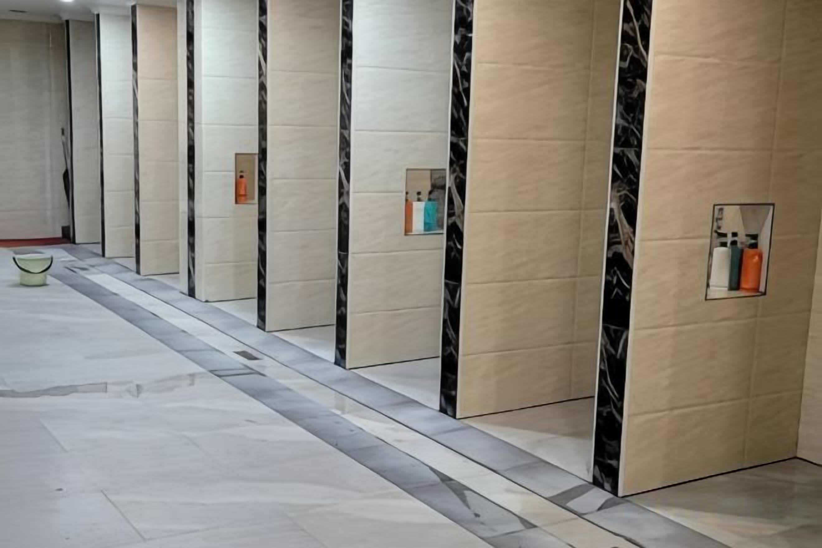Un pasillo con pisos de mármol y paredes, que conduce a habitaciones individuales con espejos y pequeños espacios de almacenamiento.