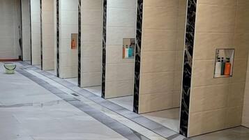 Un pasillo con pisos de mármol y paredes, que conduce a habitaciones individuales con espejos y pequeños espacios de almacenamiento.