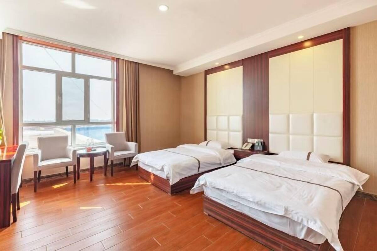Een hotelkamer met twee bedden, een bureau, stoelen en een groot raam.