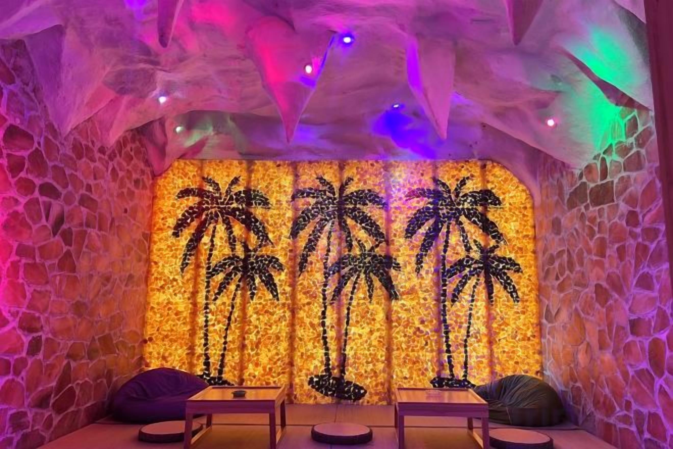 A room with a stone wall, a wall mural of palm trees, and two seating areas with tables.