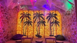 A room with a stone wall and a mural of palm trees. There are two wooden tables and two bean bag chairs.
