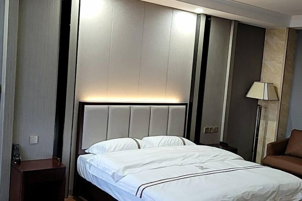 Een hotelkamer met een bed, nachtkastje, lamp en een bank.