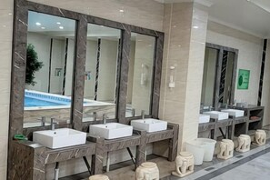 Een moderne badkamer met marmeren wastafels, grote spiegels en uitzicht op het zwembad.