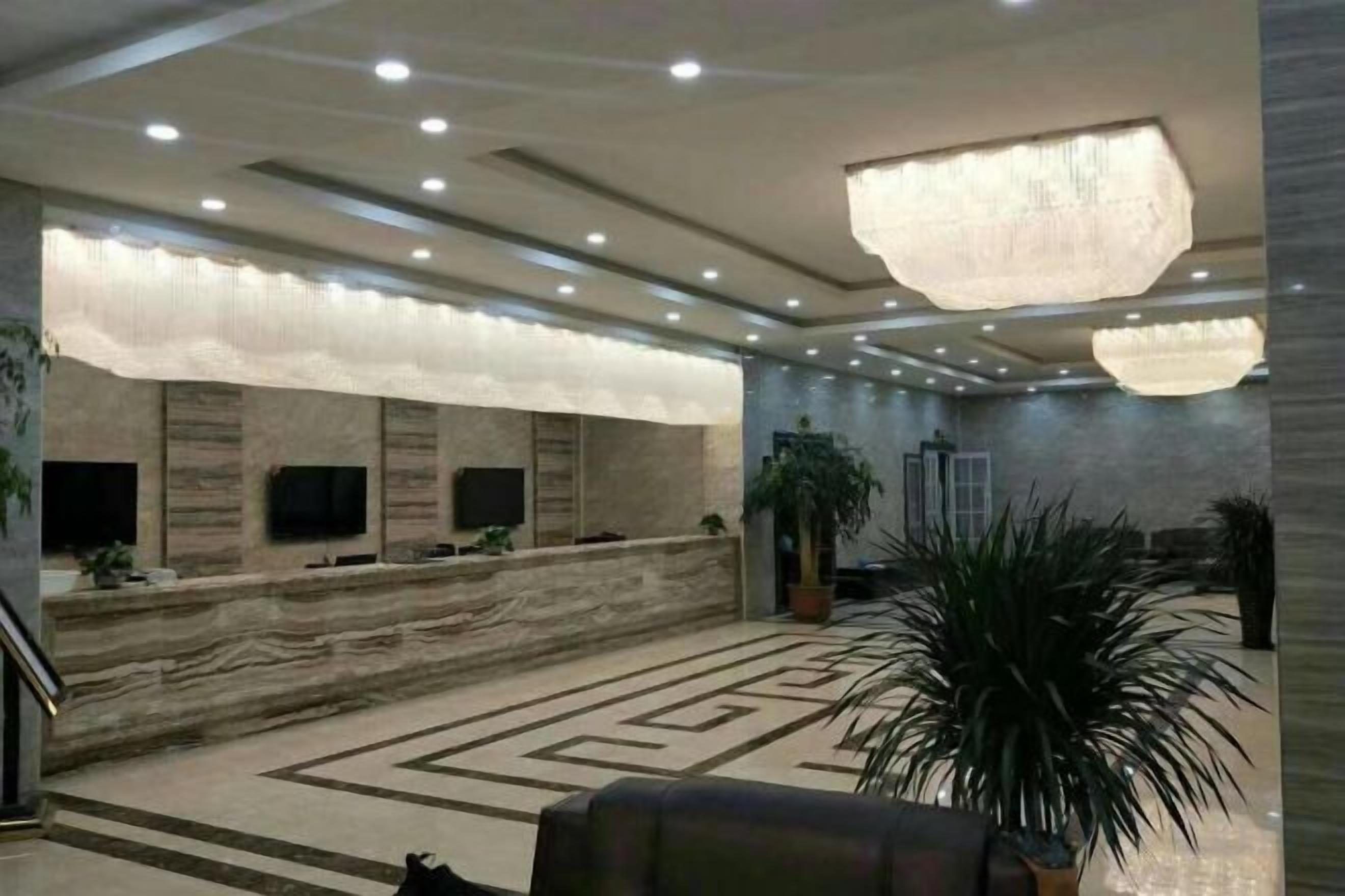A hotel lobby with a marble reception desk, multiple flat-screen TVs, a large chandelier, and a patterned carpet.
